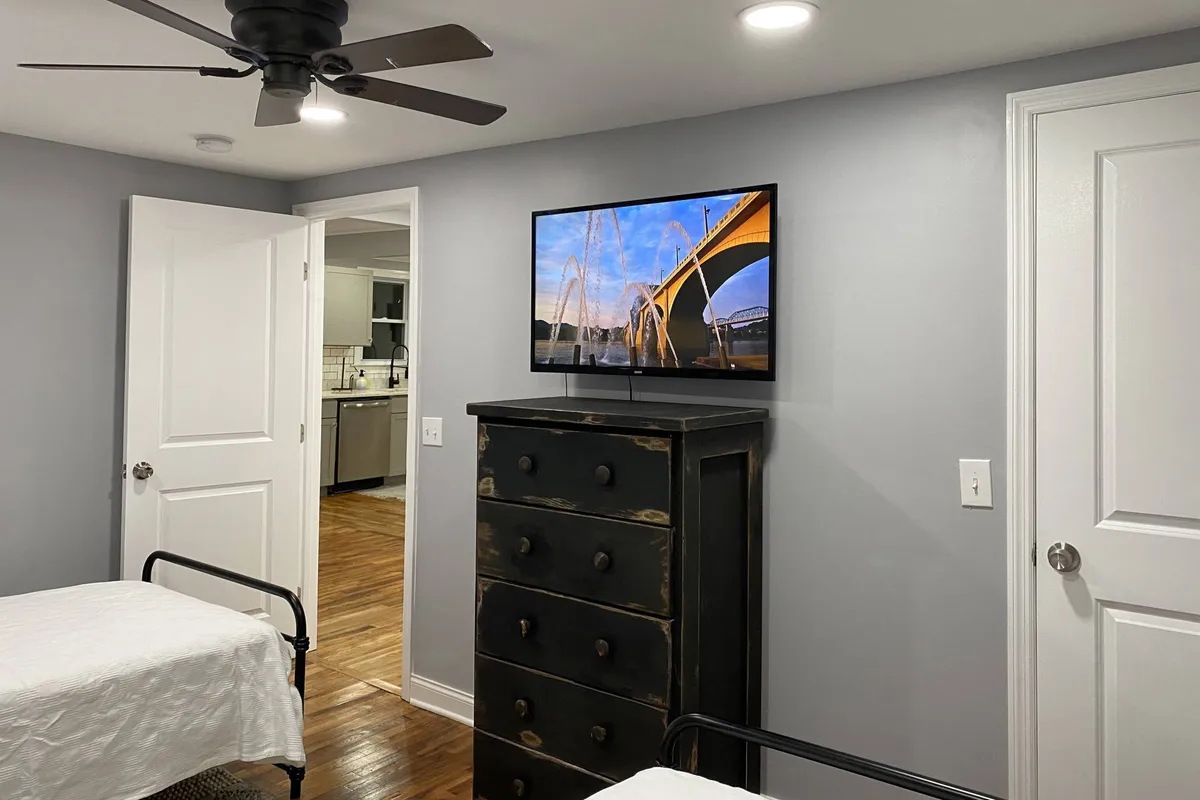 This image shows a comfortable, modern living space featuring two beds, a TV displaying a scenic bridge image, and a black dresser. The layout is open and inviting, with space for guests to relax, socialize, or plan their Chattanooga adventures. The presence of a TV hints at group-friendly entertainment like movie nights or catching up after a day of exploring nearby attractions.