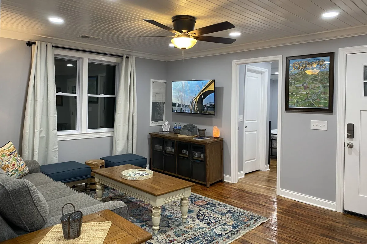 A cozy living room featuring a spacious sofa arranged around a stylish coffee table, with a TV mounted on the wall and tasteful artwork providing character. Soft curtains and accent lighting create an inviting atmosphere ideal for relaxation and social gatherings.