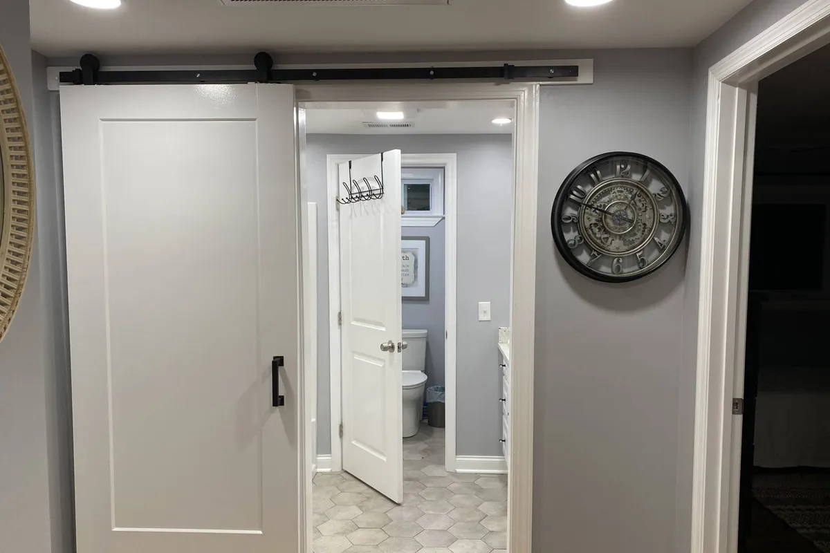 This image showcases an interior space featuring a sliding barn door, a wall clock, and hanging hooks. The atmosphere is cozy, with visual cues of morning rituals such as a coffee cup on a small table and a welcoming open feel that suggests accessibility and flow between rooms.