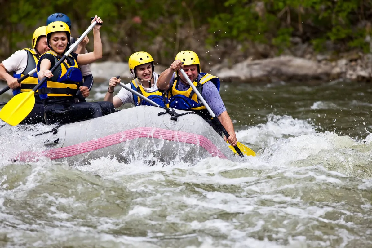 A group of people in a rafting boat paddling down a lively river, surrounded by lush greenery. The image exudes excitement, teamwork, and an adventurous spirit.