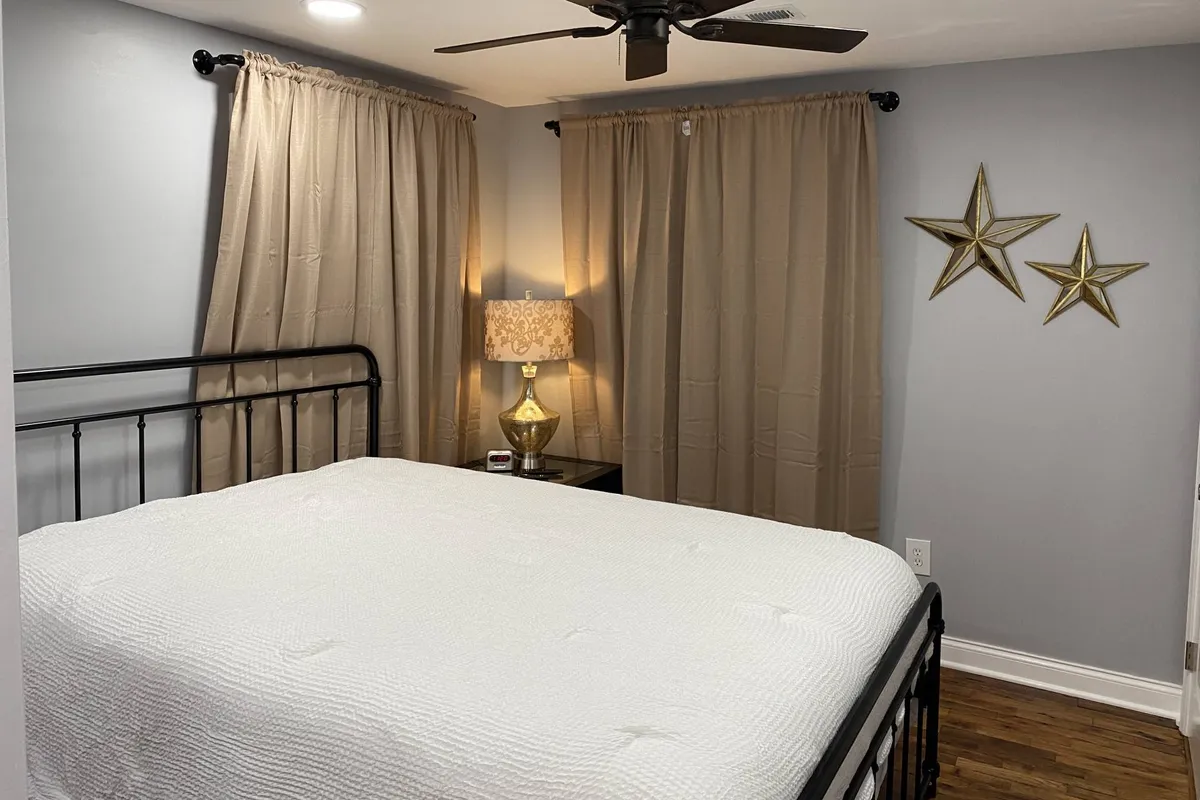 A single metal-framed bed is positioned by a window with soft curtains, accompanied by a decorative lamp and whimsical star decorations. The room captures a quiet, peaceful mood, enhanced by natural morning light filtering through the fabric, suggesting both relaxation and readiness for a productive day.