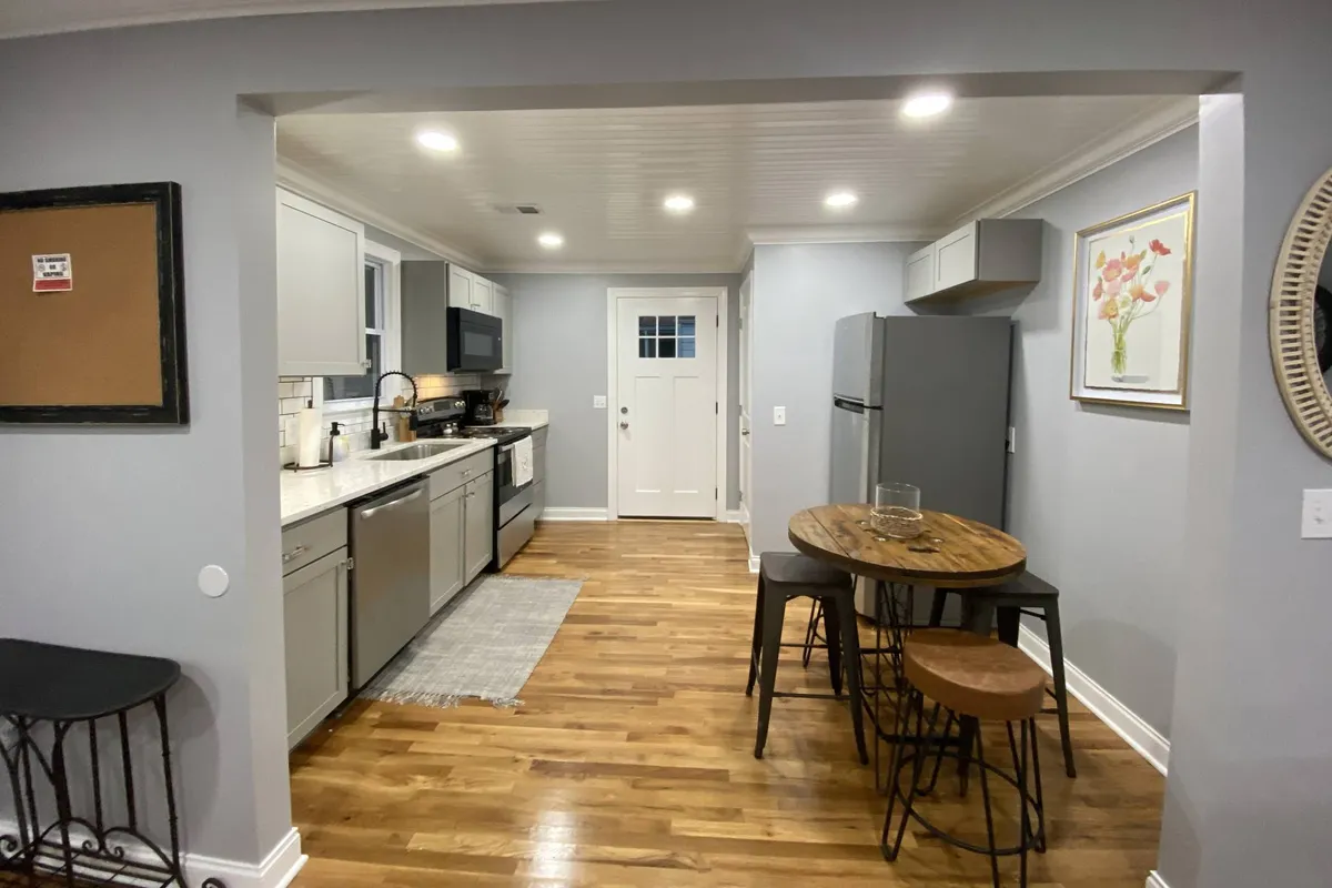 A modern kitchen area with a large island, sleek stools, and visible appliances, flowing into the dining space. The setup is open and welcoming, ideal for meals, snacks, or group conversations.